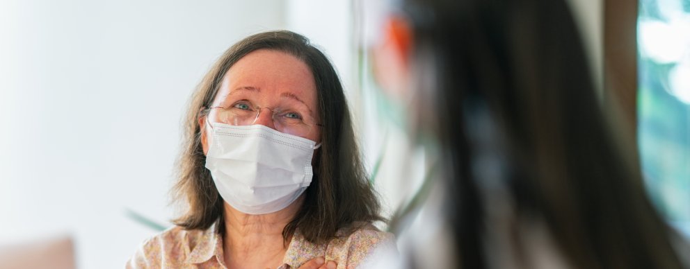 Woman in mask looking at a provider thankfully and holding her hand over her heart